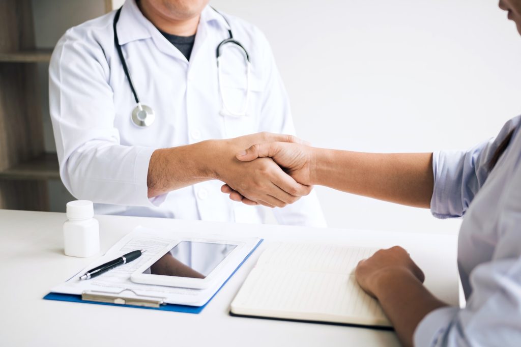 Doctor shaking hands with older patient in the clinic room.